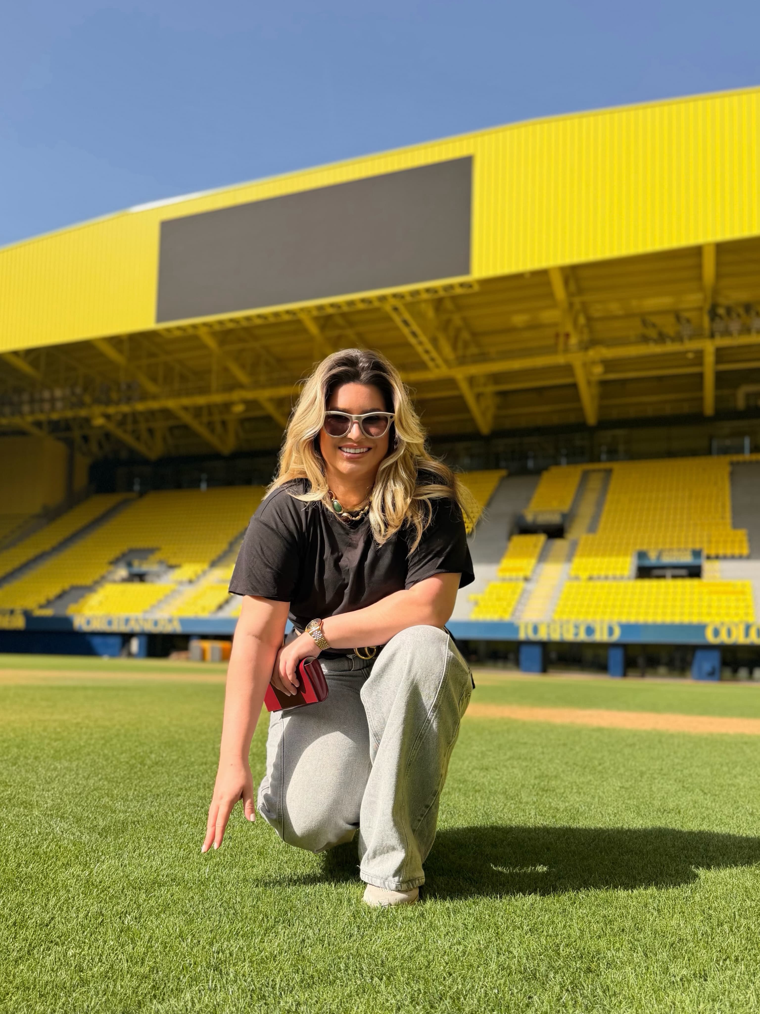 Carla Larini agachada no gramado de um estádio